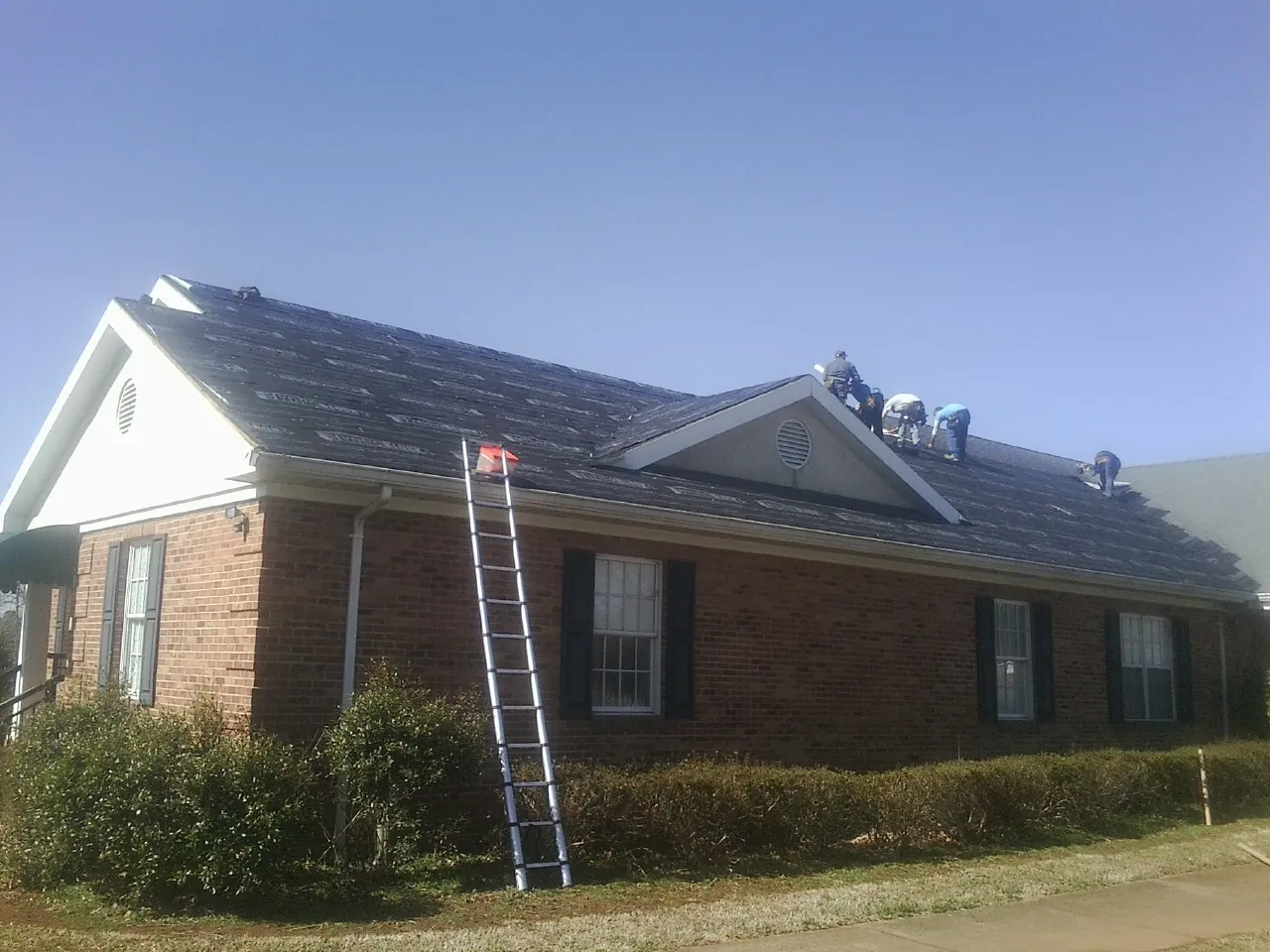 Crew tearing shingles off a brick ranch roof with a ladder set — Metal Roof Repair work by our crew in Falmouth