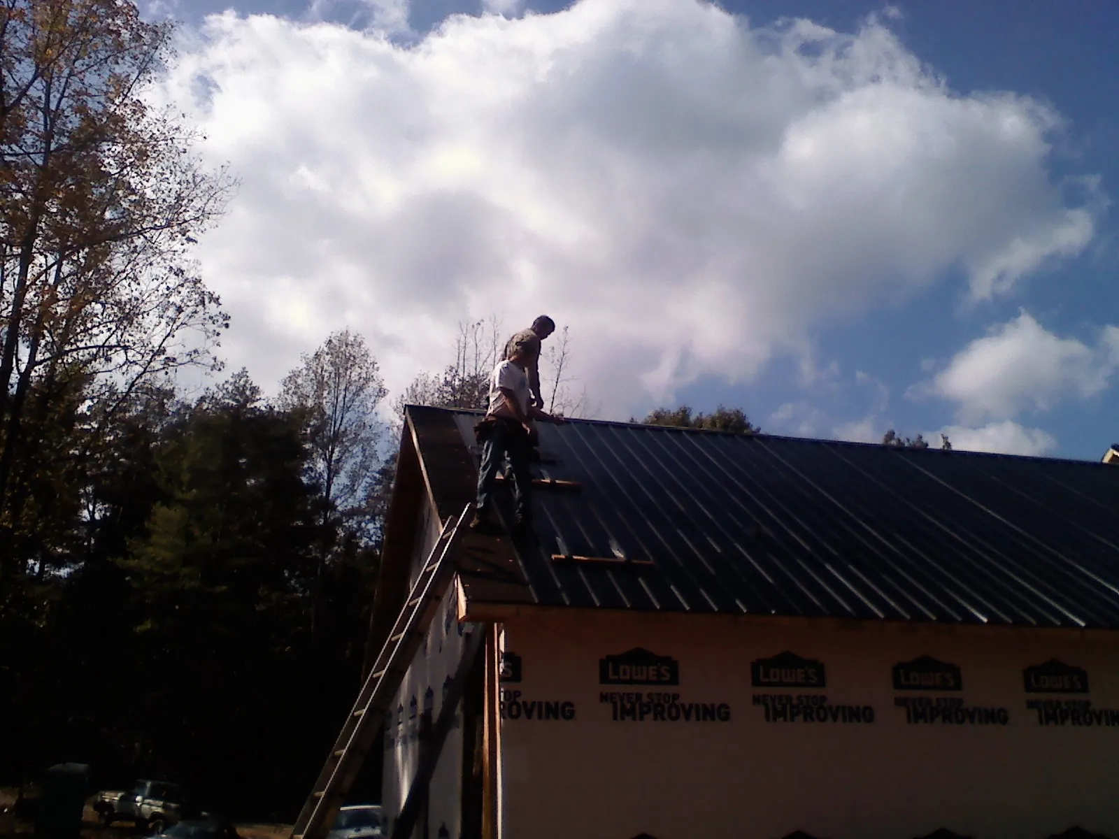 Roofer fastening dark metal panels high against a cloudy sky, from a Roof Inspection job in Falmouth