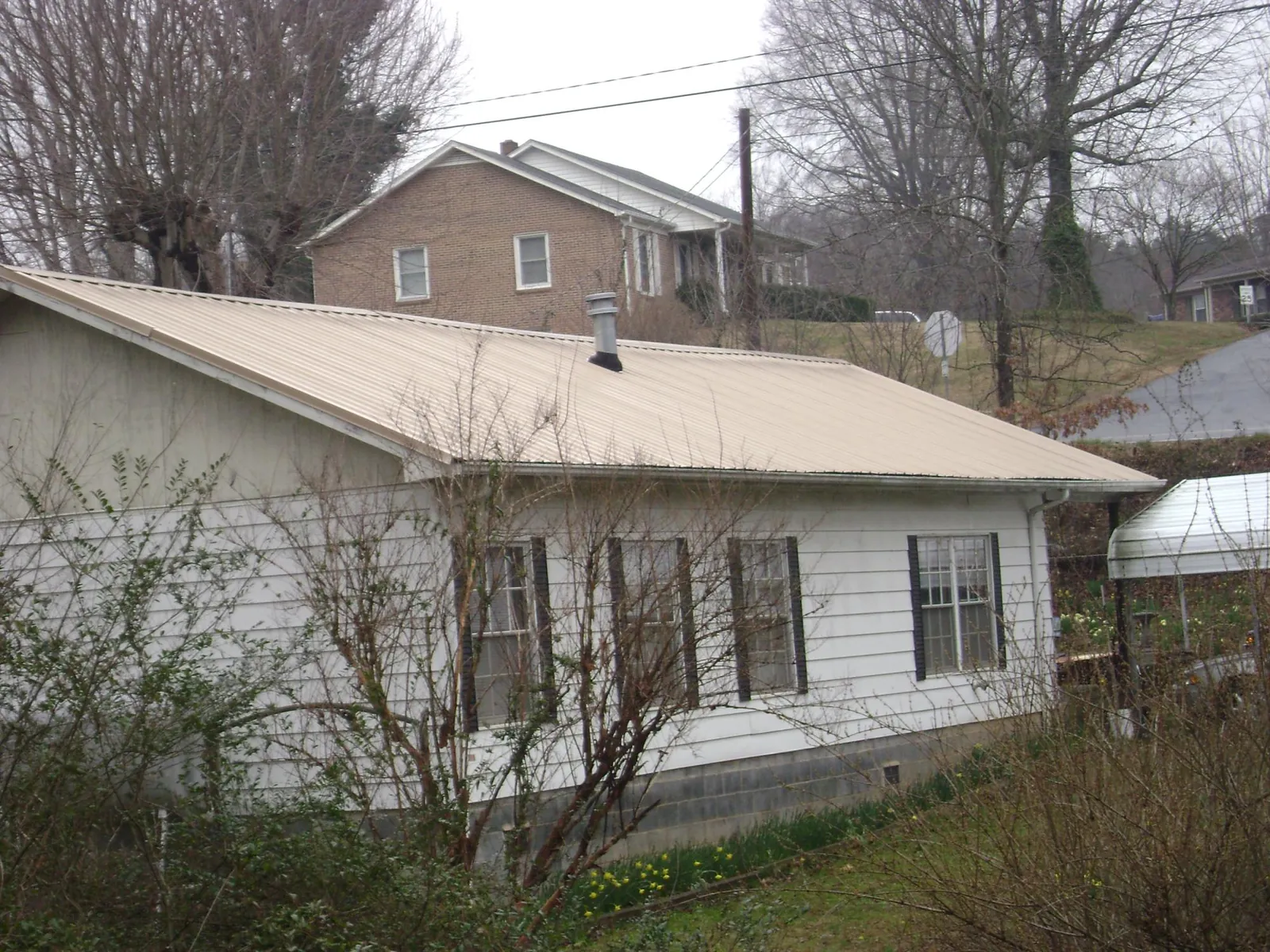 Tan metal roof on a white sided house set into a hillside — Commercial Roofing by Roofing Brothers in Falmouth